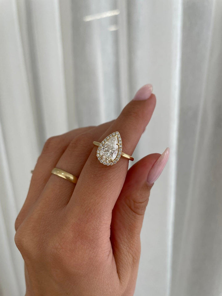a woman's hand holding a ring with a pear shaped diamond